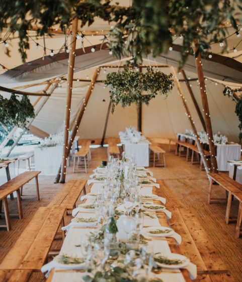Inside The Big Hat TipisComplete with rustic refectory tables, long wooden benches, twinkly lights & greenery.